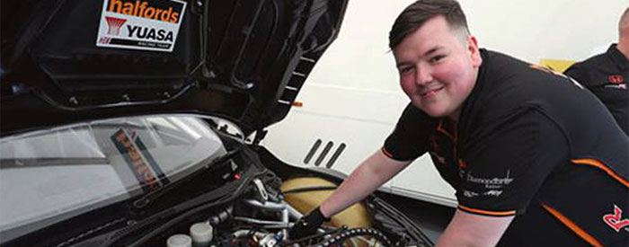 Josh Hall standing over a car's engine and smiling